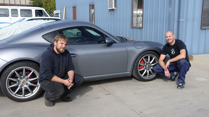 Image of Chris and Steve kneeling in front of a silver Porsche.